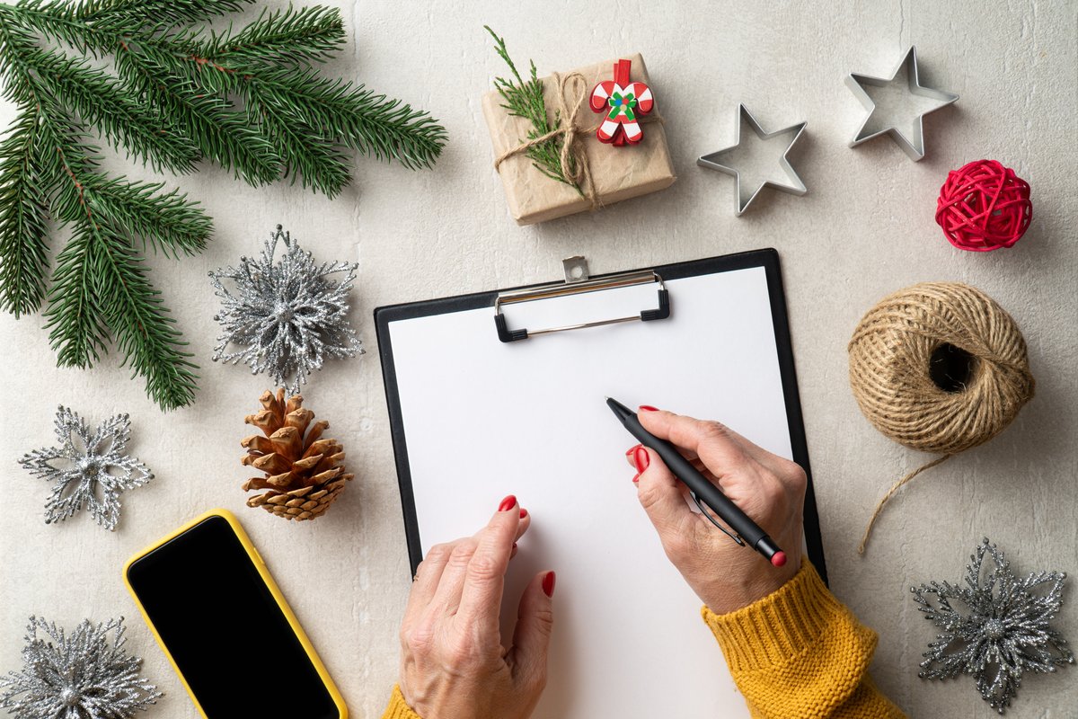 Hands writing a holiday shop planning checklist on a clipboard surrounded by holiday decorations